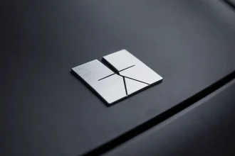Gros plan sur un emblème de marque automobile minimaliste en chrome mat sur carrosserie noire, illustrant la tendance à l'épuration des logos de voiture