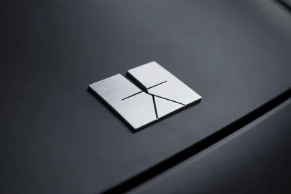Gros plan sur un emblème de marque automobile minimaliste en chrome mat sur carrosserie noire, illustrant la tendance à l'épuration des logos de voiture