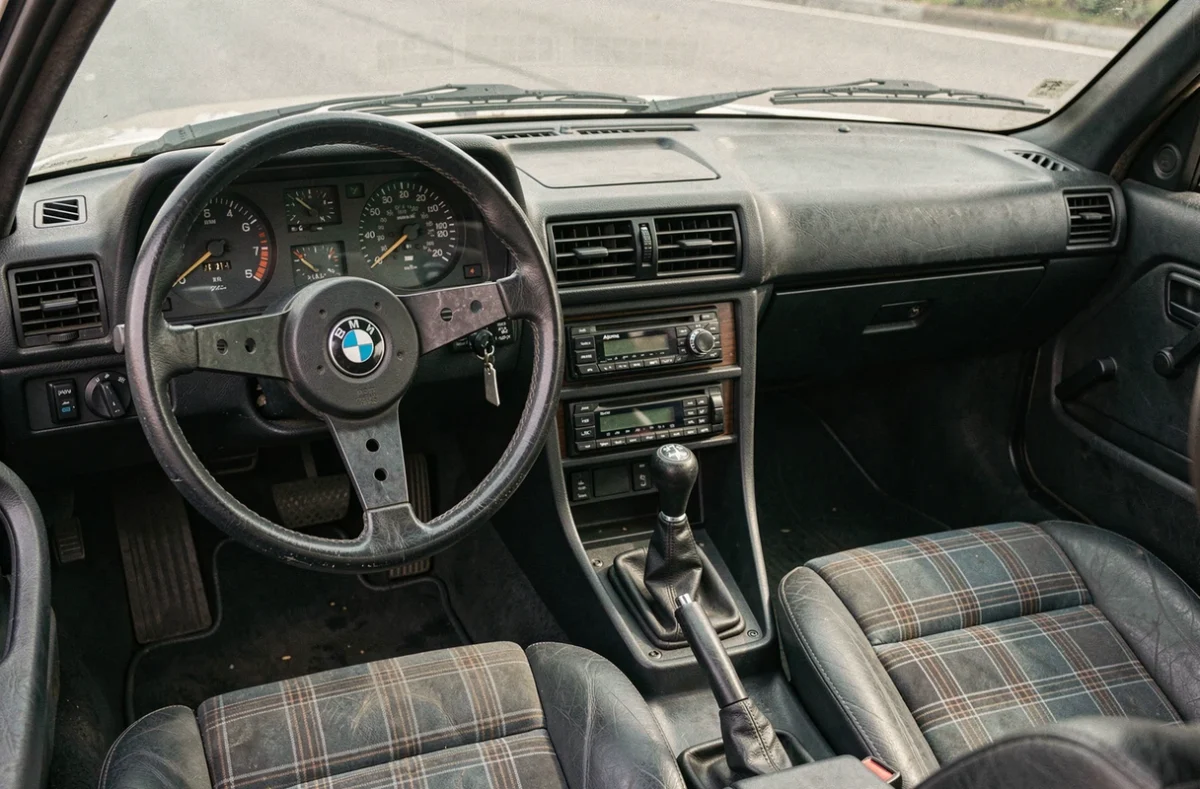 Intérieur authentique d'une BMW E30 de 1990 avec volant trois branches, tableau de bord analogique et sièges à carreaux sportifs