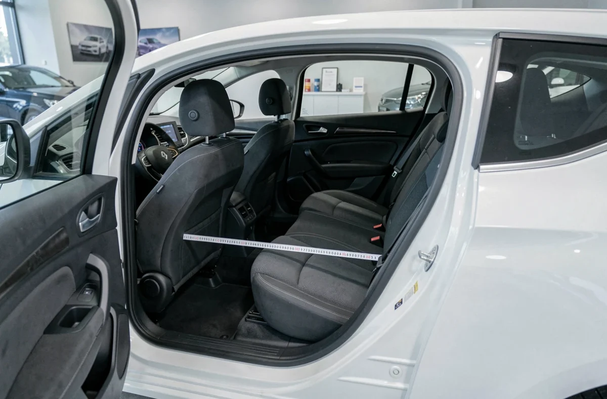 Intérieur d'une Renault Megane blanche avec un mètre ruban mesurant l'espace aux jambes arrière dans un showroom