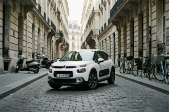 Nouvelle Citroën C3 blanche effectuant un virage serré dans une rue pavée étroite d'une ville européenne
