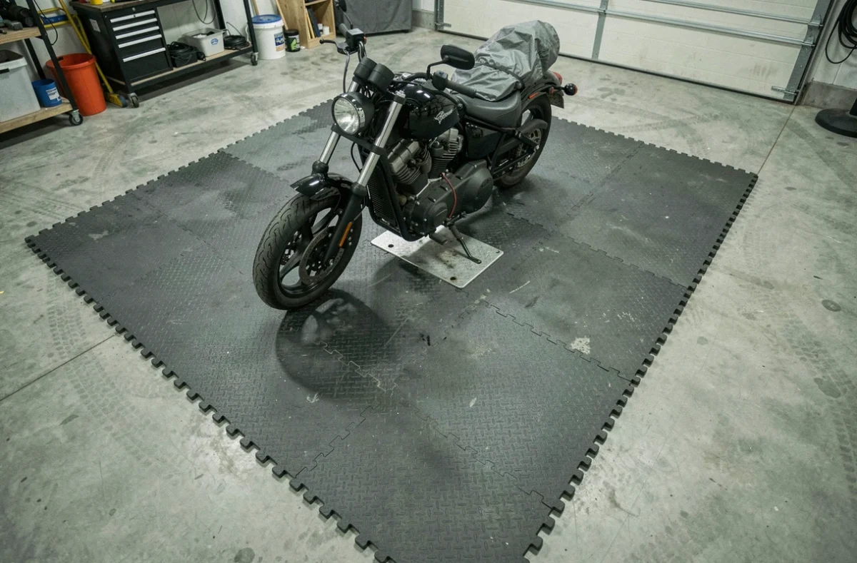 Vue en plongée d'un tapis modulable en mousse pour garage moto avec chargeur de batterie connecté et bac récupérateur d'huile, configuration complète pour hivernage